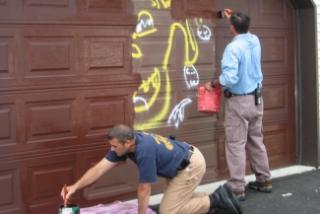 Captain Mike Vangelo and Chief Larry Palmer paint a garage on the City’s Southside